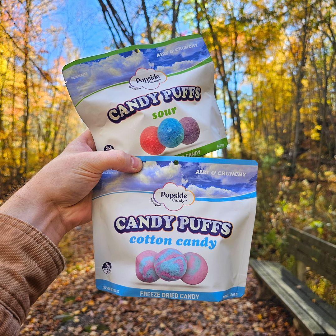 Freeze dried candy bags held up in air with colorful fall leaves in the background.
